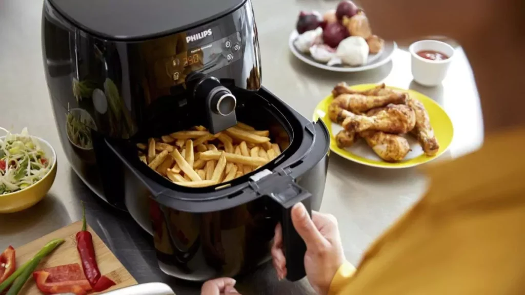 Mão abrindo cesto de air fryer com batatas fritas