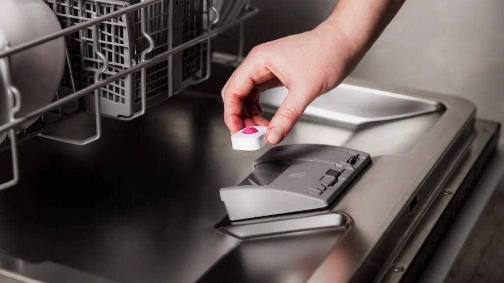 Mão inserindo tablete de detergente para lava louças em compartimento de insumos