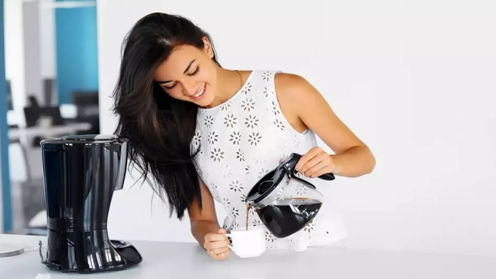 Mulher servindo café coado com uma cafeteira elétrica