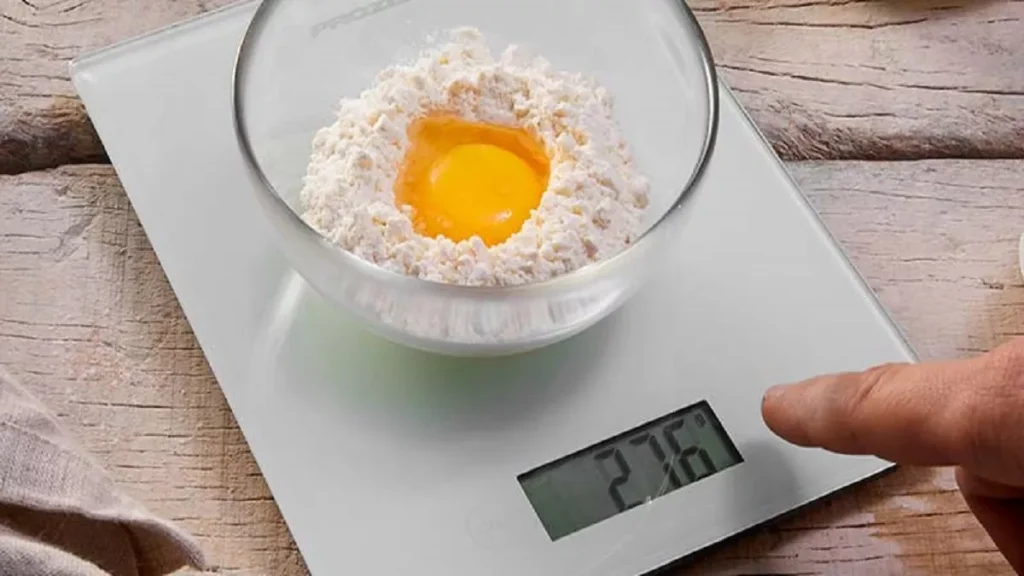 Pessoa pesando ovo e farinha em uma balança de cozinha